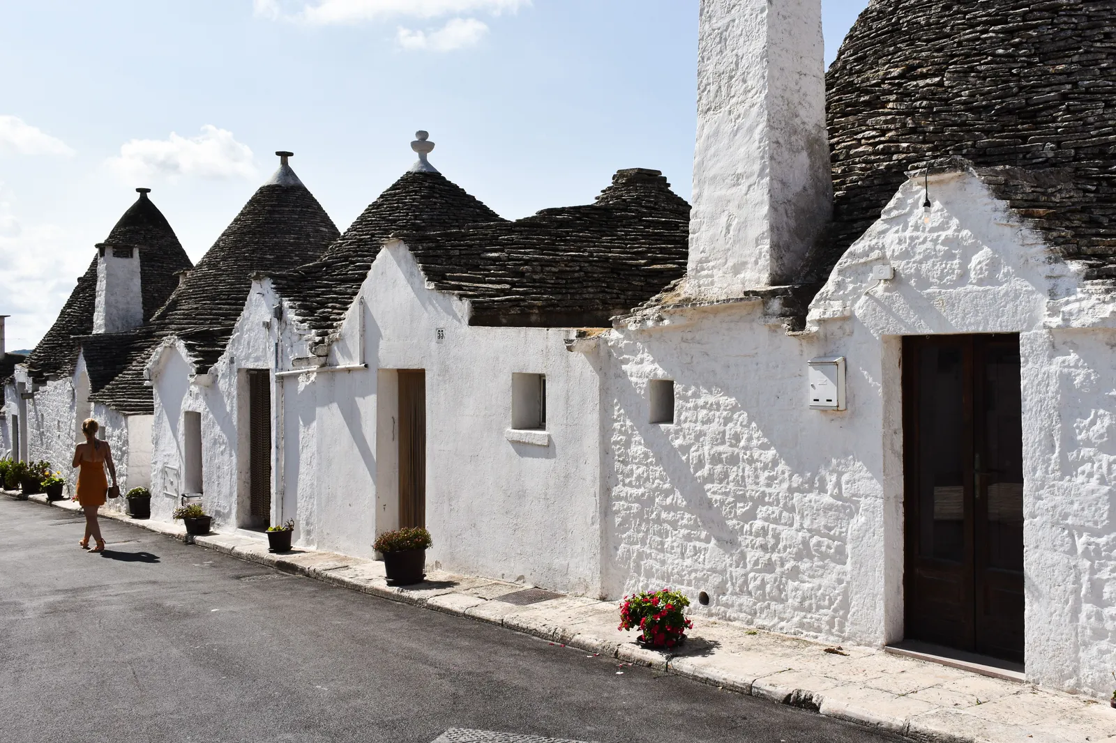 A street of whitewashed trulli houses with a woman walking past in Alberobello, Italy