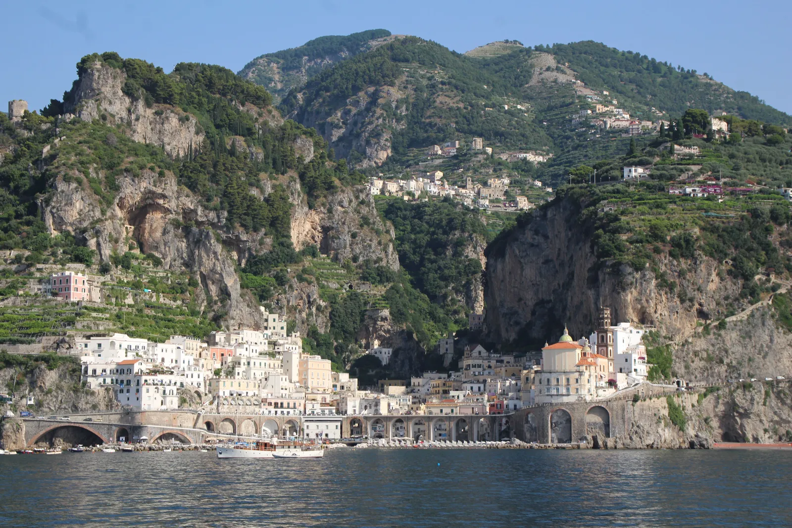 A winding coastal road above a sparkling blue sea and terraced cliffs on the Amalfi Coast