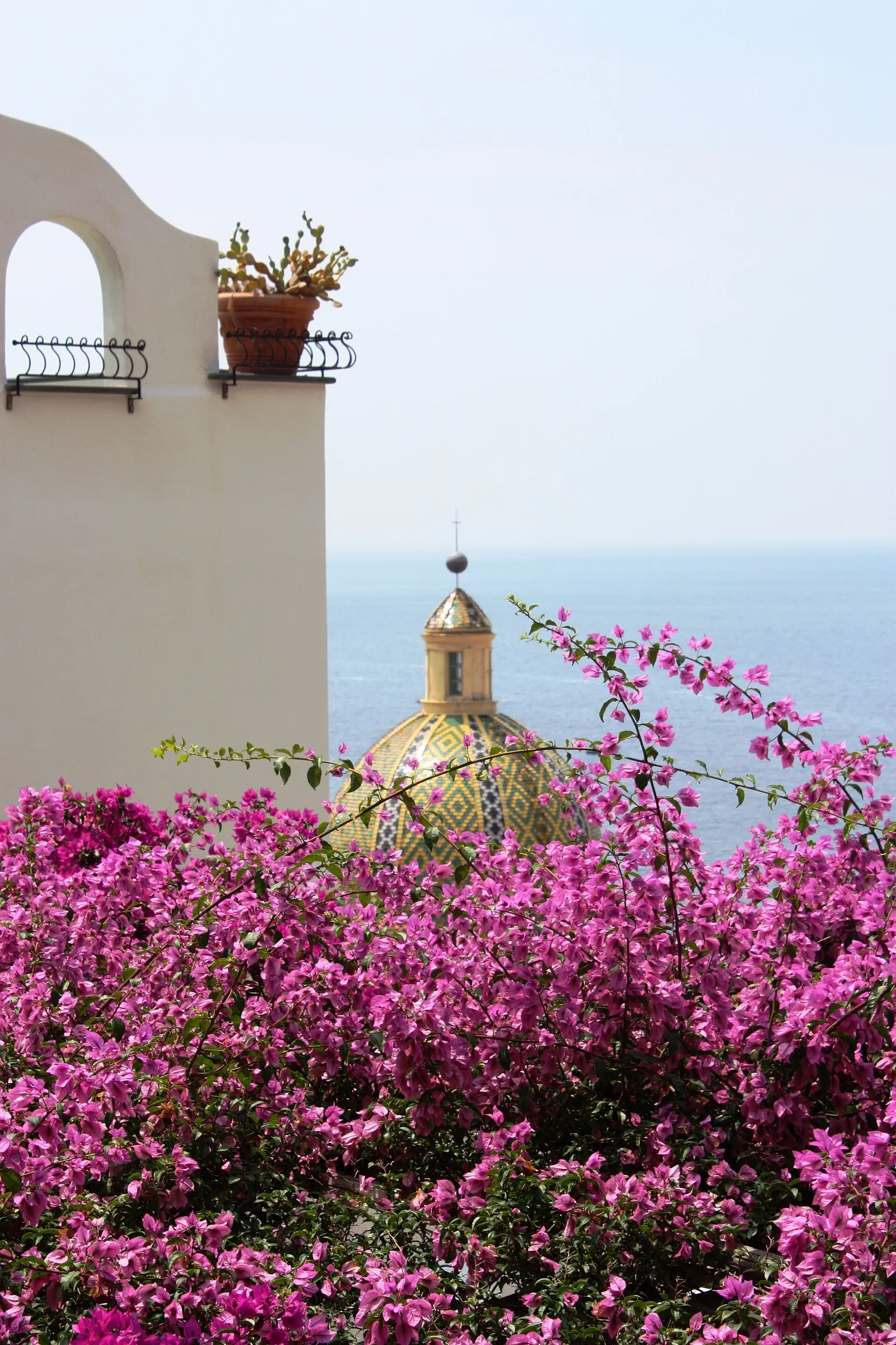 The tiled dome of the Positano church framed by pink bougainvillea above the sea on the Amalfi Coast, Italy