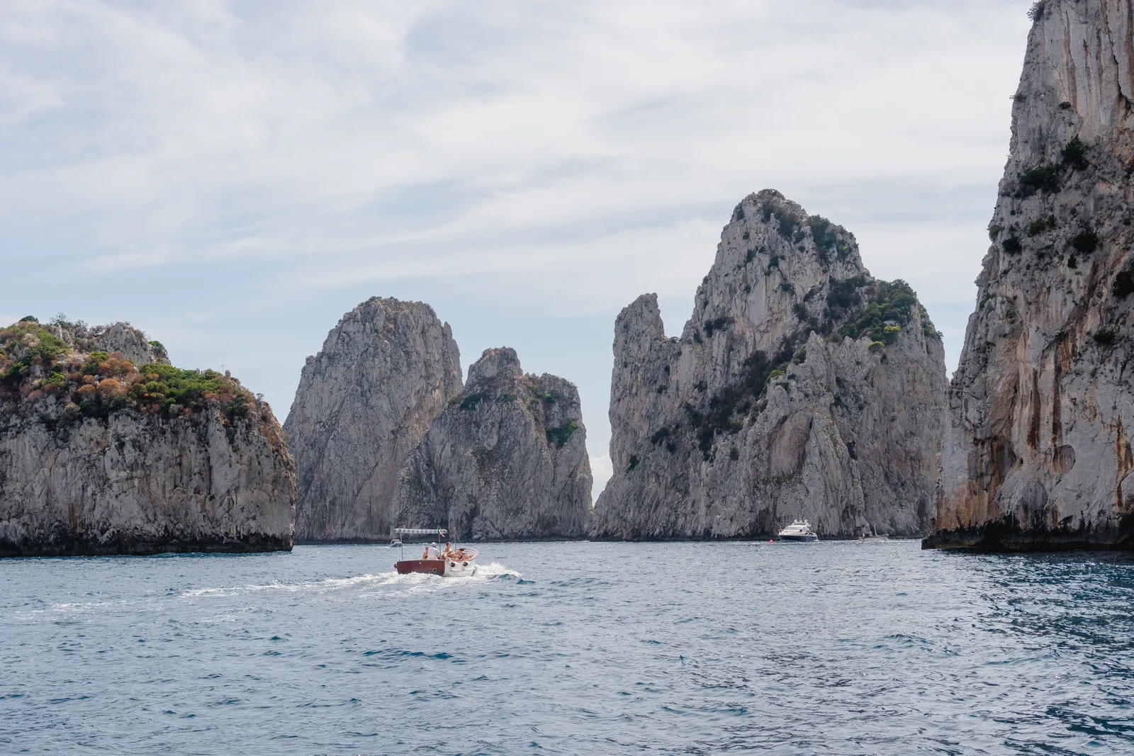 The Faraglioni sea stacks off Capri with a small boat passing between them, Italy