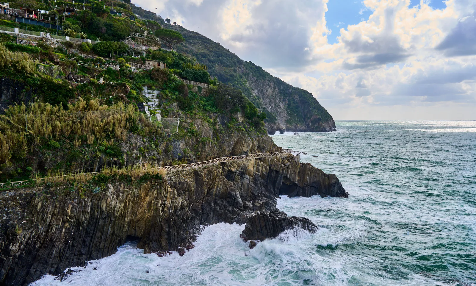 A railed coastal footpath cut into the cliffs above the sea in Cinque Terre, Italy