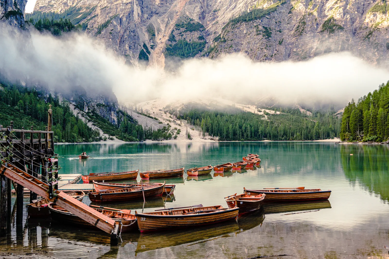 Jagged pale peaks reflected in an emerald alpine lake with a wooden boathouse in the Dolomites, Italy