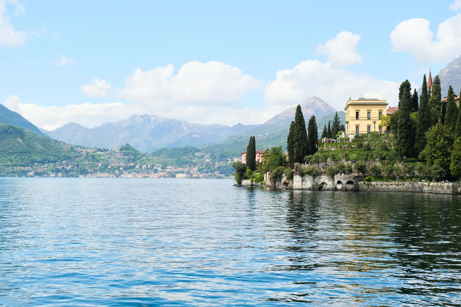 Lakeside villas and cypress trees along the shore of Lake Como with mountains behind
