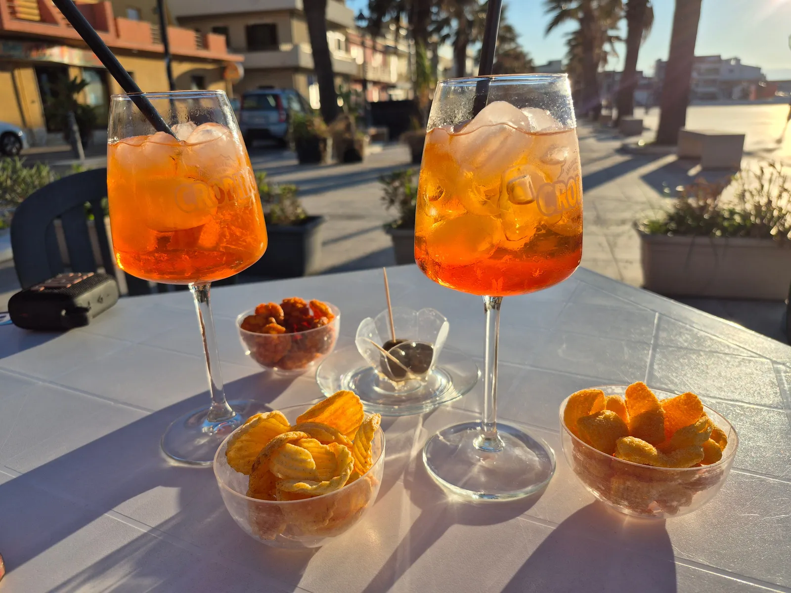 Two spritz glasses and small bowls of snacks on an outdoor bar table in Italy