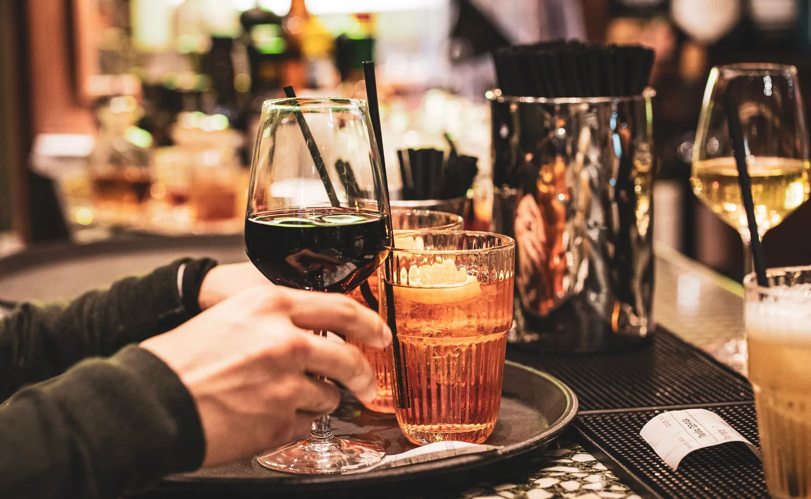 A hand reaching for a glass of red wine beside a spritz on a bar tray