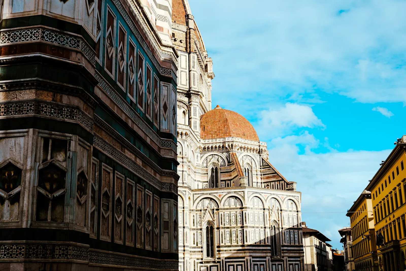 A sunlit piazza with a fountain and outdoor cafe tables in a historic Italian city centre