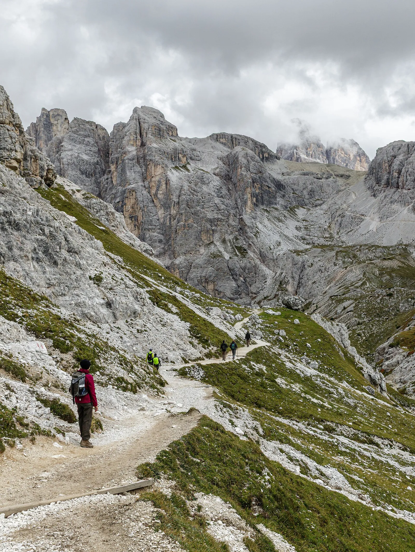 Hikers on a high mountain trail beneath grey limestone peaks in the Dolomites, Italy