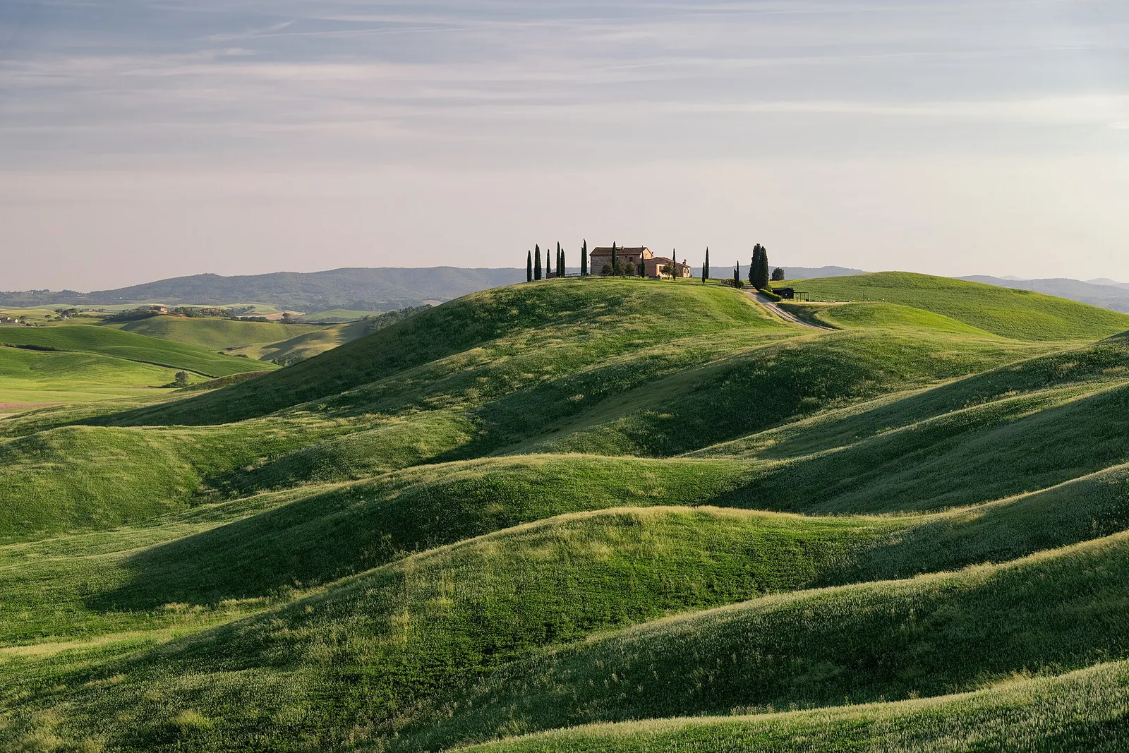 Green rolling hills of Tuscany in spring with a stone farmhouse and cypress trees under a soft sky