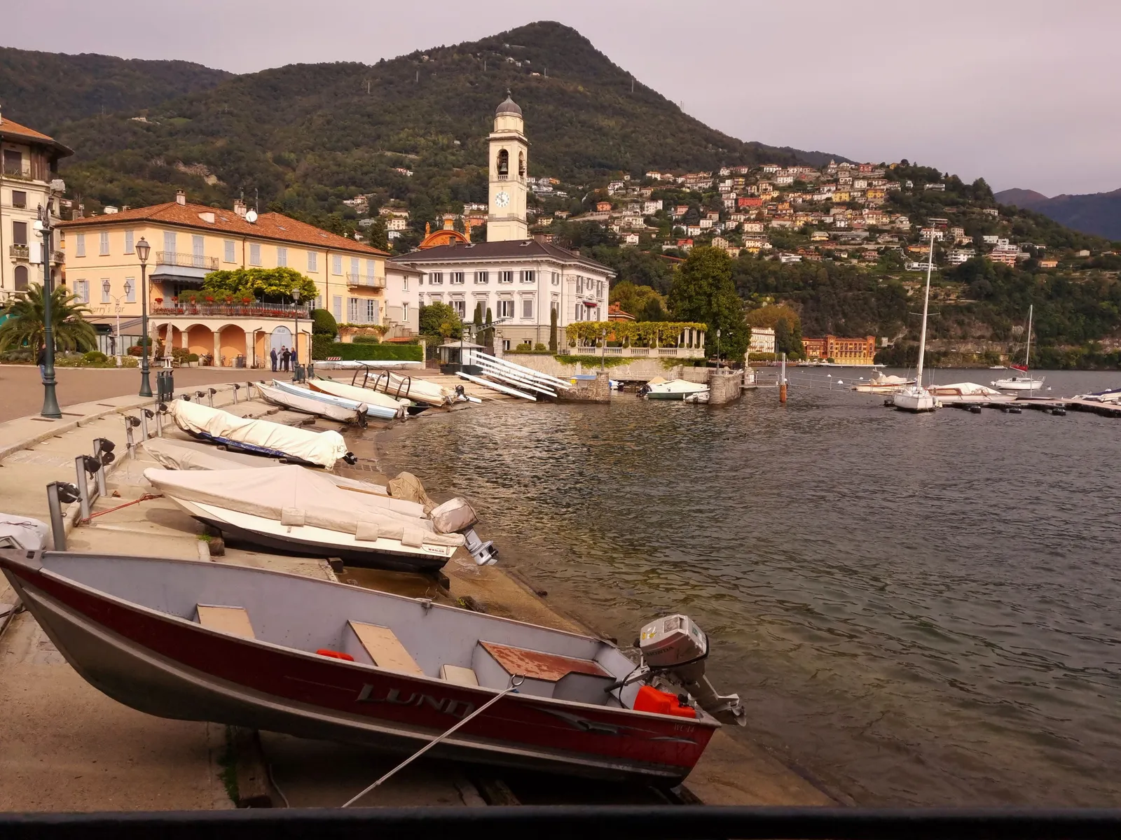 A lakeside village with boats moored below wooded mountains on Lake Como, Italy
