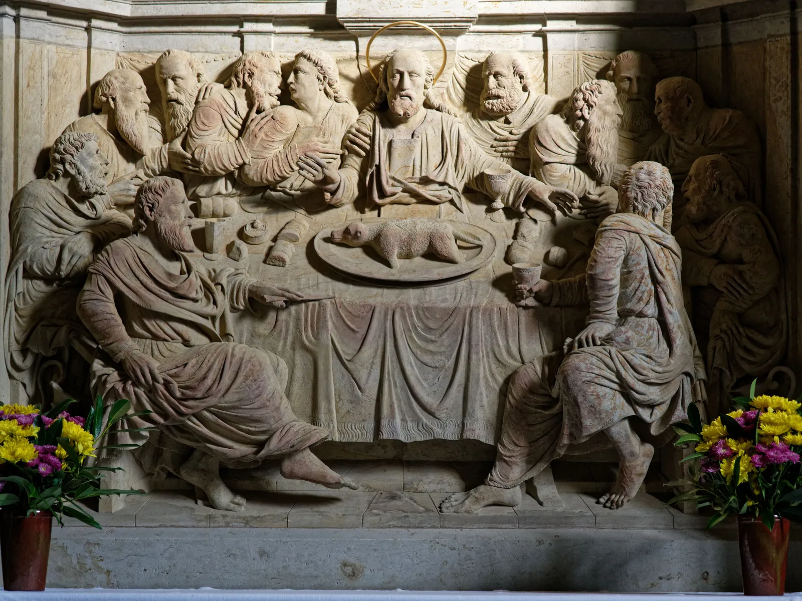 A stone relief of the Last Supper scene with flowers in front of it in Milan, Italy