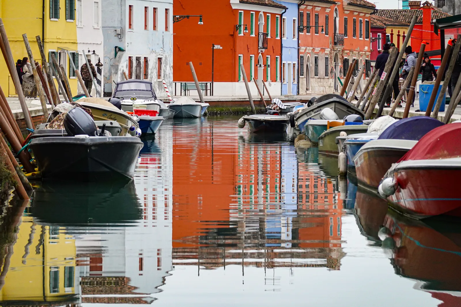 Boats moored in front of painted houses reflected in the water at Burano, Italy