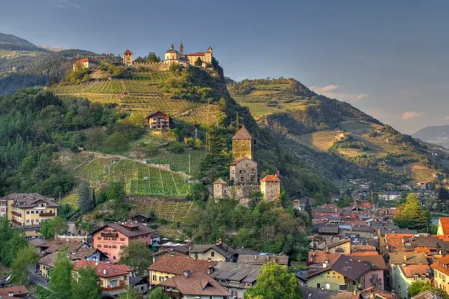 A hillside town of red tiled roofs below a fortress on a green ridge