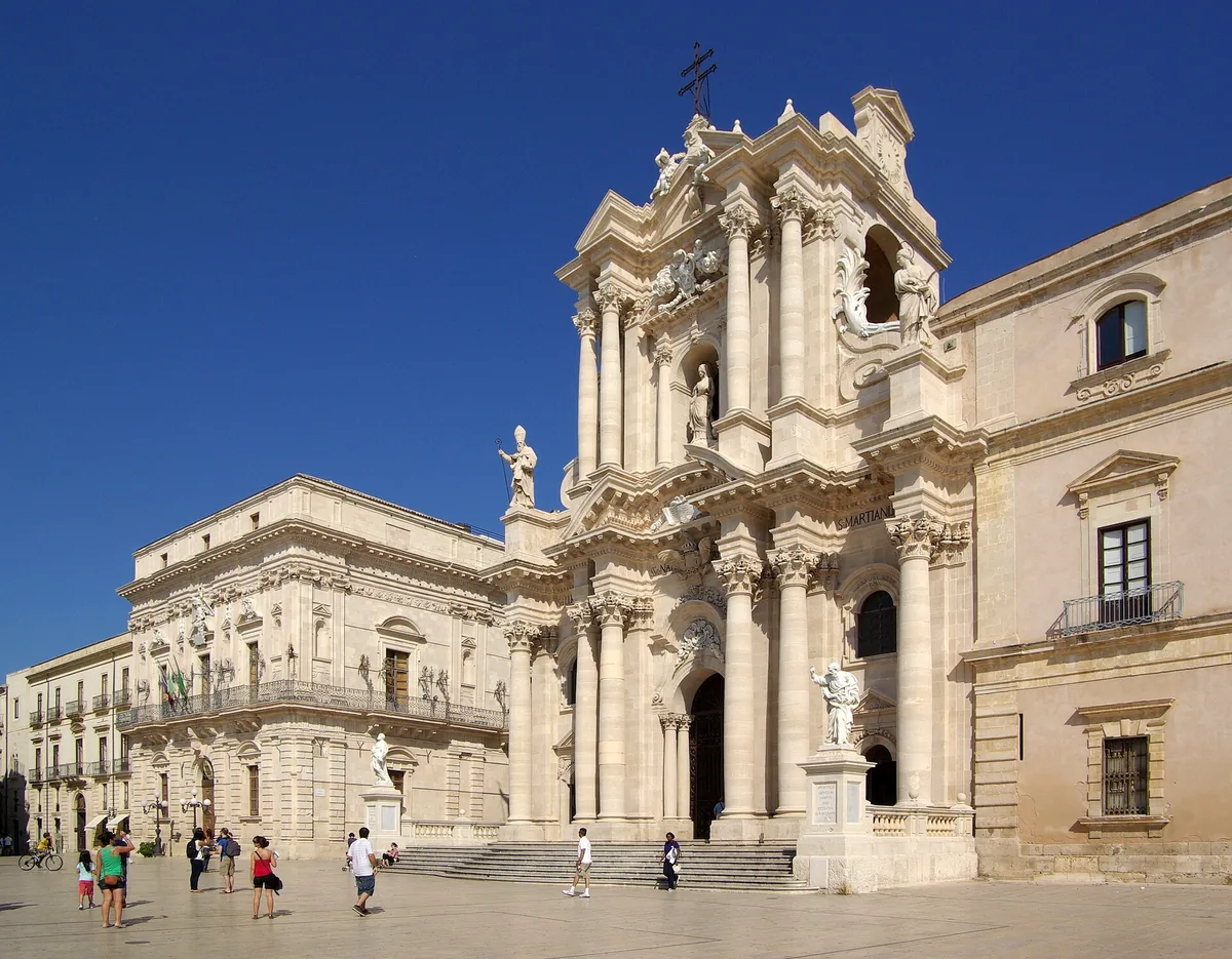 Baroque cathedral facade with columns and stone statues against a deep blue sky