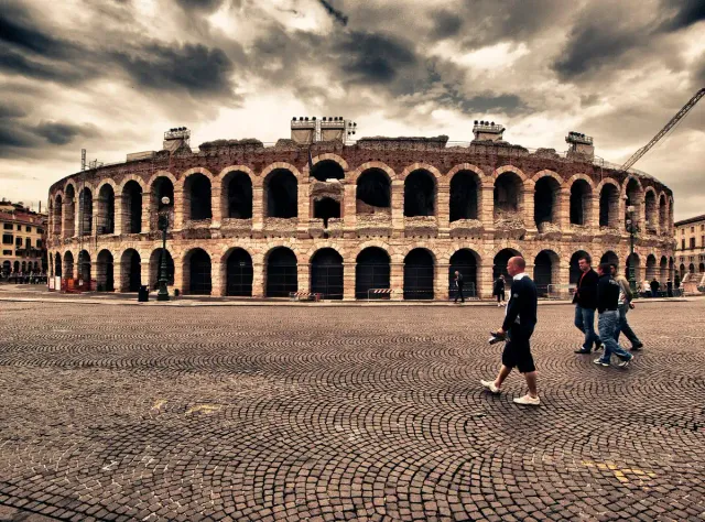 A Roman amphitheatre of pink stone with tiered arches above a paved square