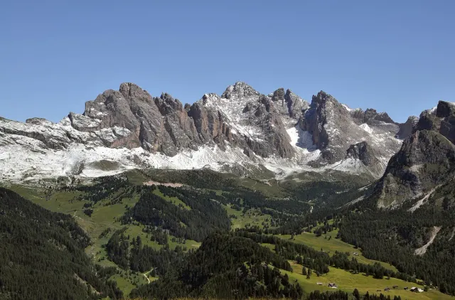 Jagged Dolomite peaks rising above green meadows and forested slopes