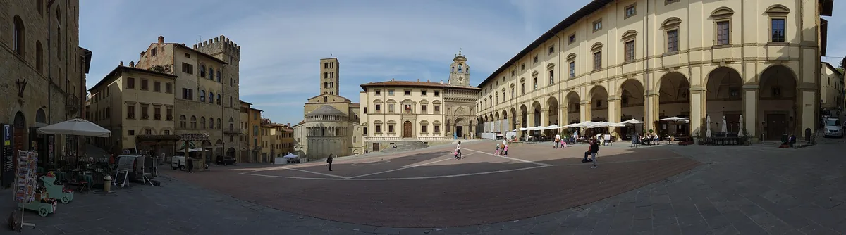 A sloping brick paved square ringed by stone palaces and an arcaded gallery