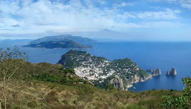 A high view over a blue bay, white cliffs and a town climbing the slope