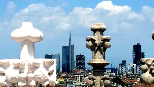 Carved marble spires on a cathedral roof against modern glass towers