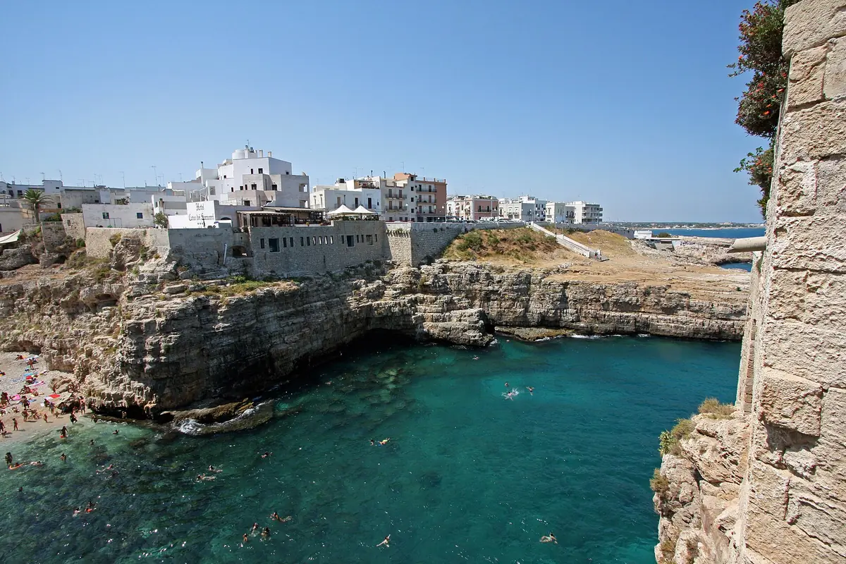 A small turquoise cove between white limestone cliffs with whitewashed houses along the clifftop