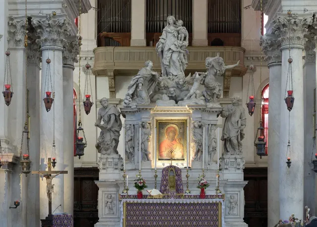 A marble altar with white statues framed by columns in a bright church