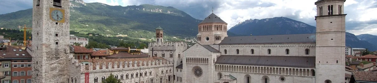 A pale stone cathedral with a tower and dome, green mountain slopes rising behind it