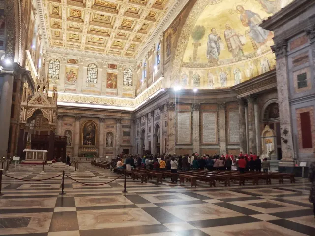 A vast church interior with a gilded coffered ceiling and rows of marble columns