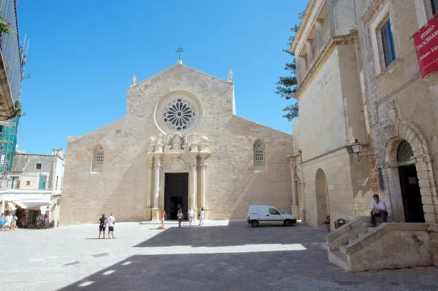 A pale stone church facade with a rose window above a paved square