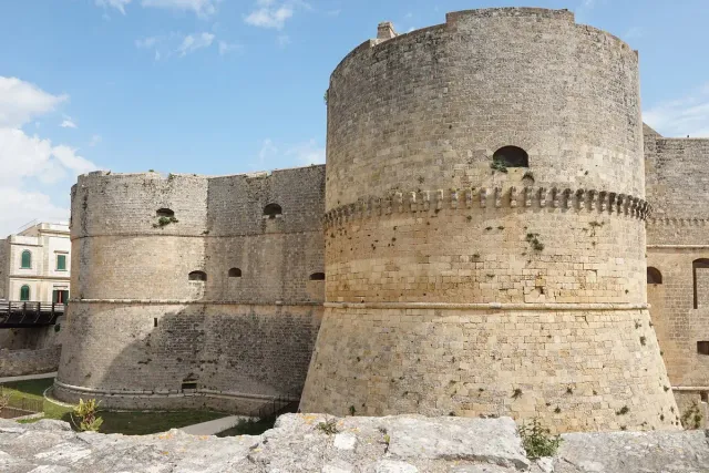 A round brown stone fortress with thick walls above a dry moat