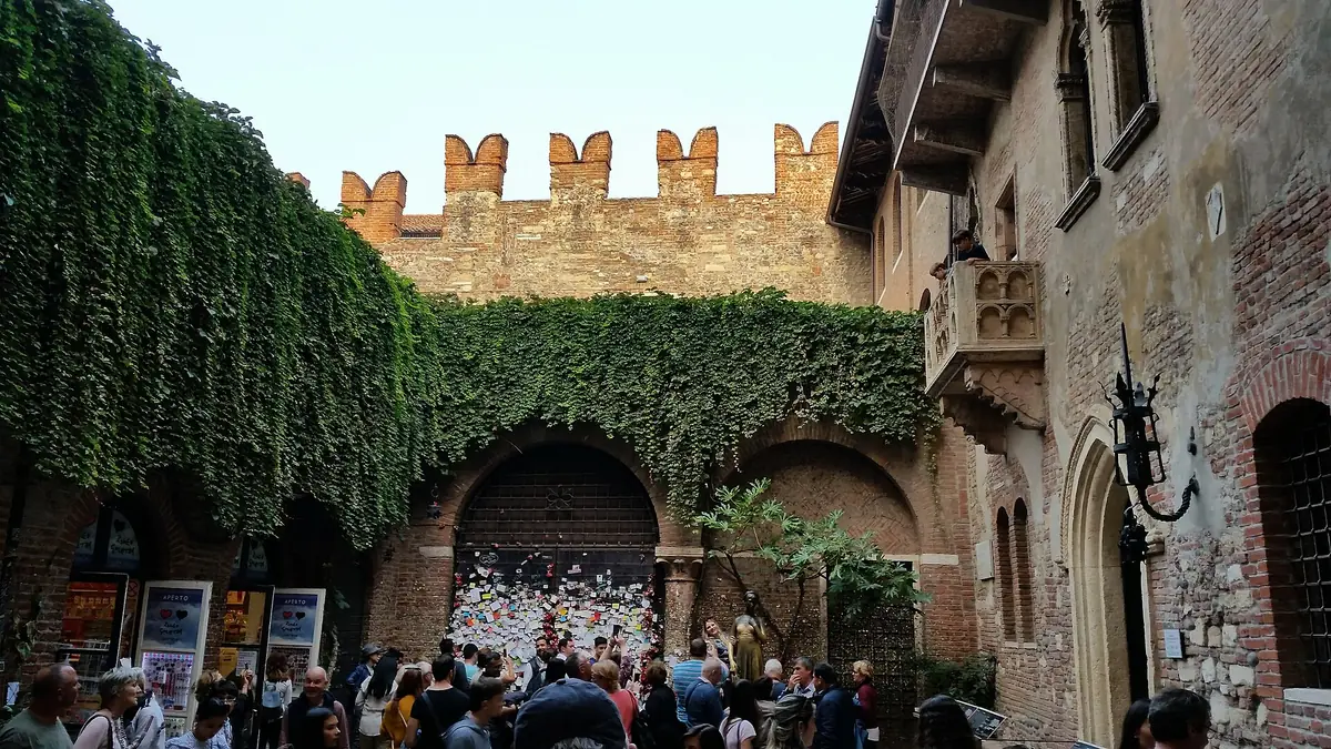 Paved courtyard framed by ivy covered walls, a stone balcony and a crenellated wall