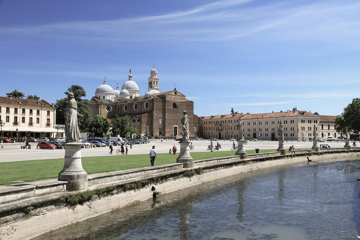 An elliptical water canal lined with stone statues beside a green lawn
