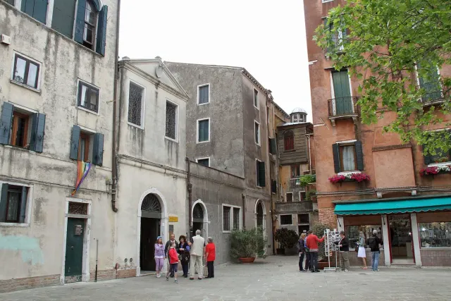 A broad square ringed by tall stone houses with visitors by a museum doorway