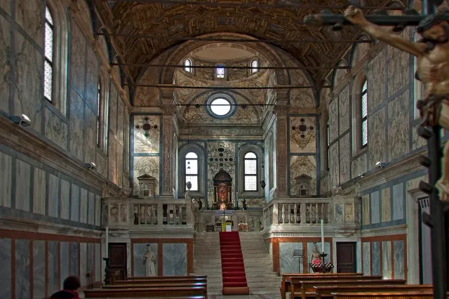 A narrow marble church interior with a painted ceiling and steps to the altar