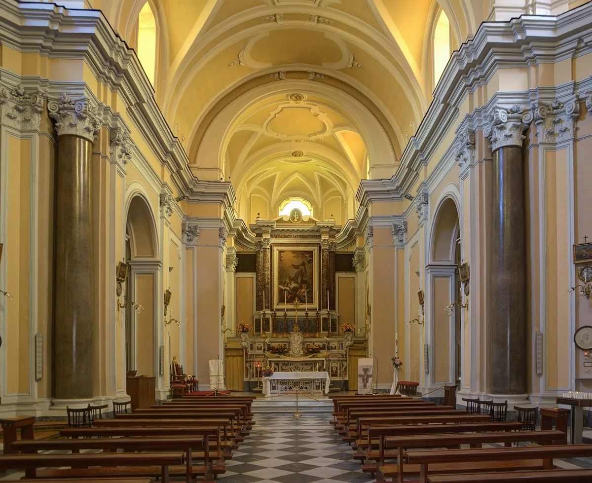 A church nave with tall columns, a vaulted ceiling and a lit marble altar