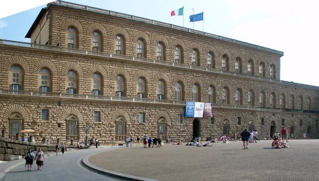 A long rusticated stone palace facade above a sloping square