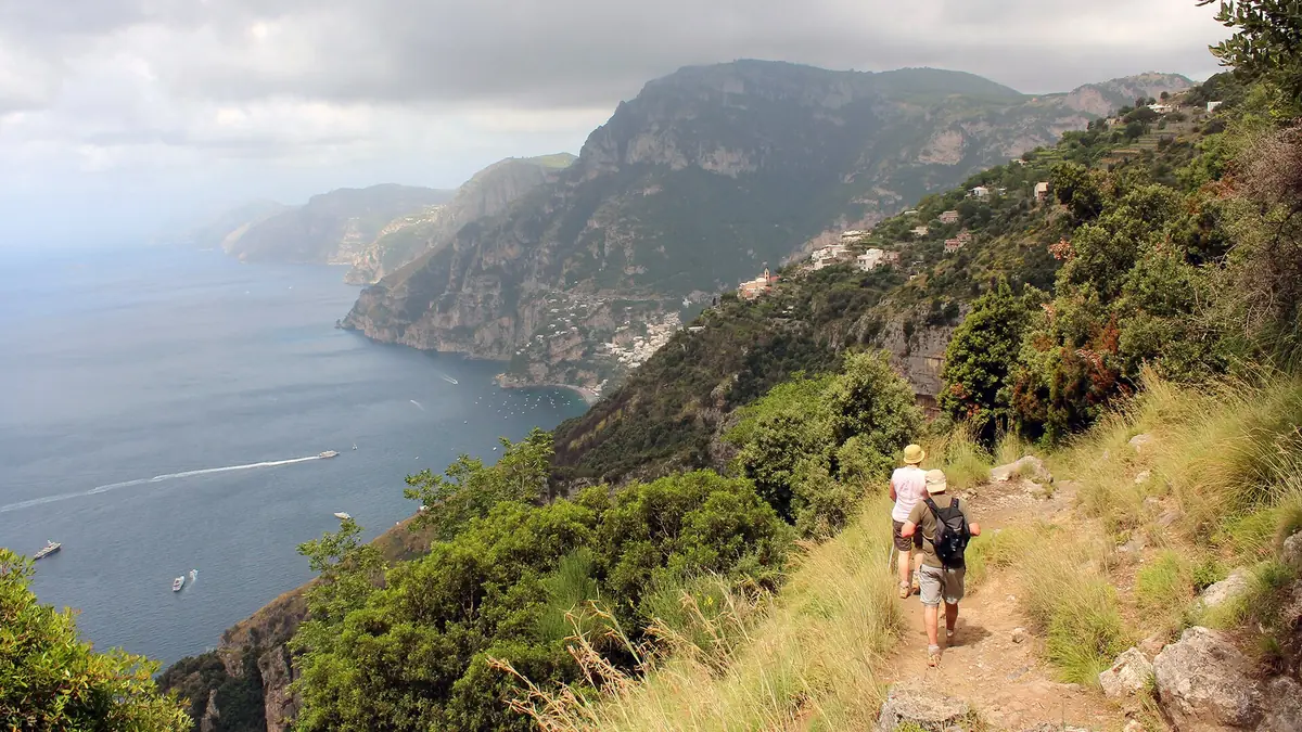 A narrow dirt path on a green slope above cliffs dropping to the sea
