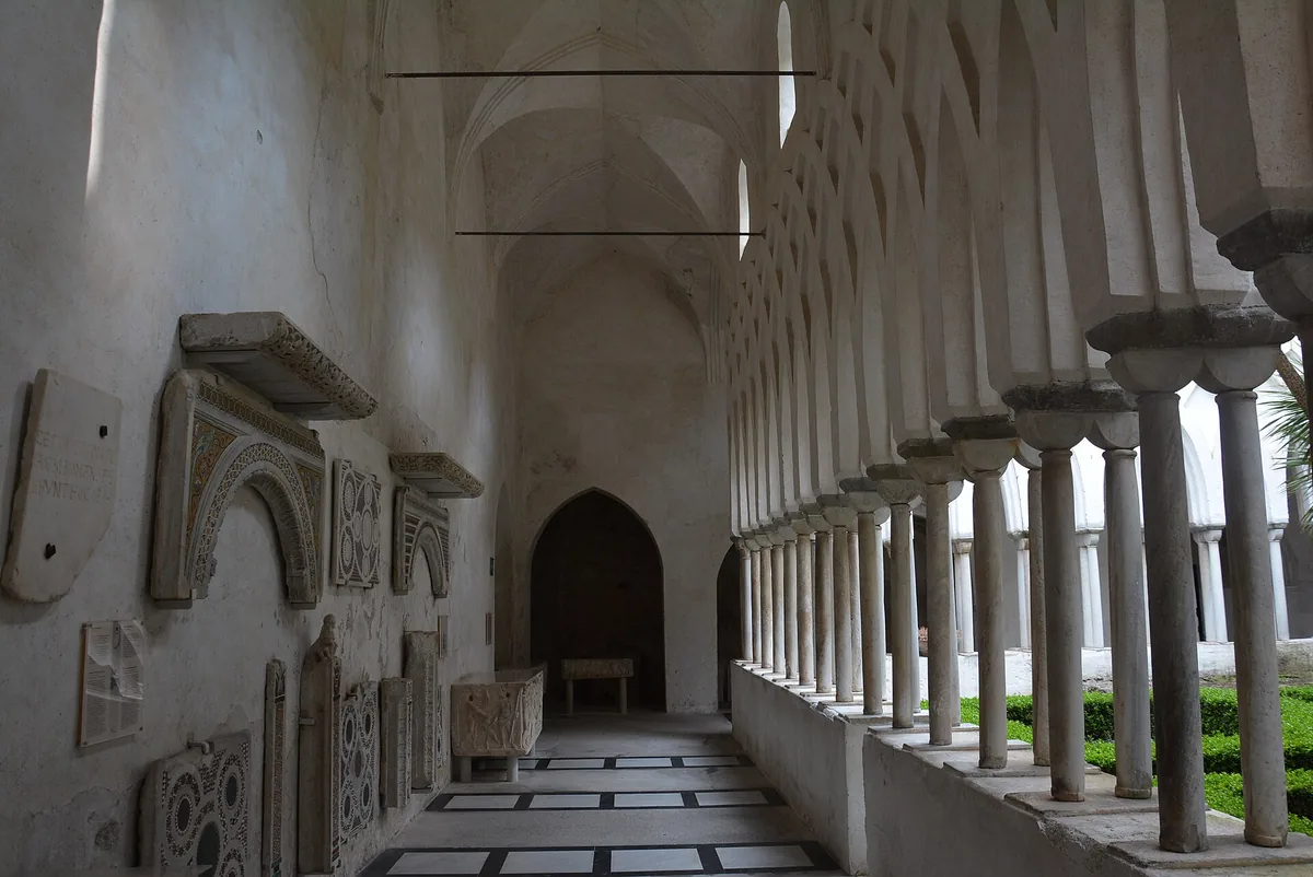 A cloister walkway of slender white columns and pointed arches facing a courtyard