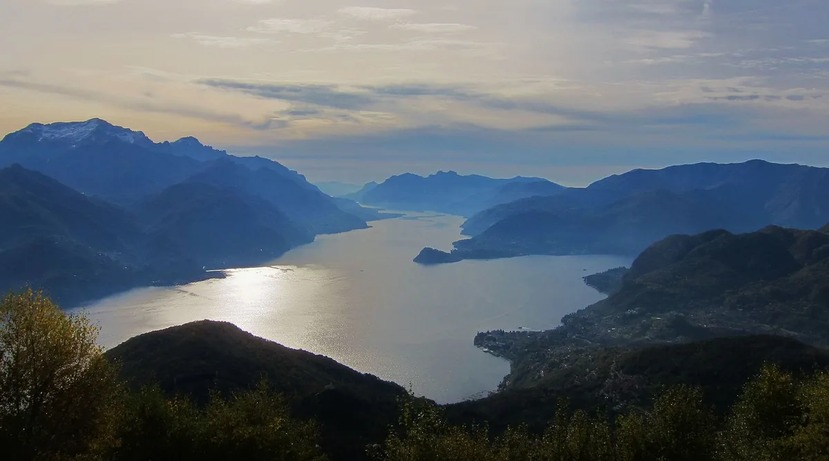 A narrow lake between bluish mountain ridges with light reflecting on the water
