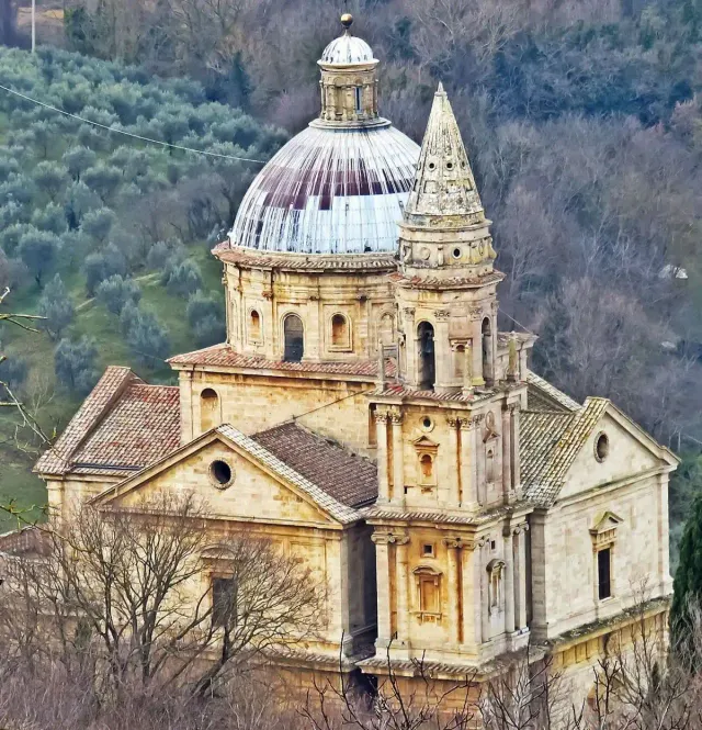 A pale stone Renaissance church with a dome and tower among Tuscan fields