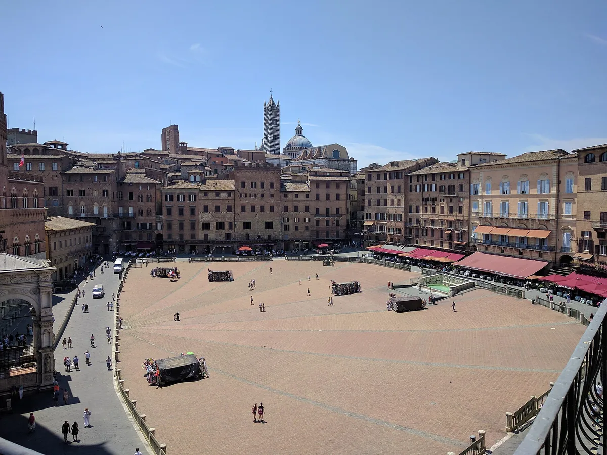 A fan shaped brick paved square ringed by stone houses, with a bell tower behind