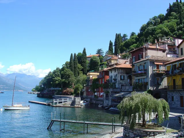 Colourful houses at the lake edge with a white boat and mountains behind