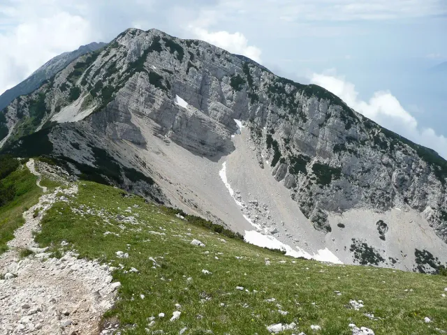 A rocky mountain ridge with green slopes and patches of snow