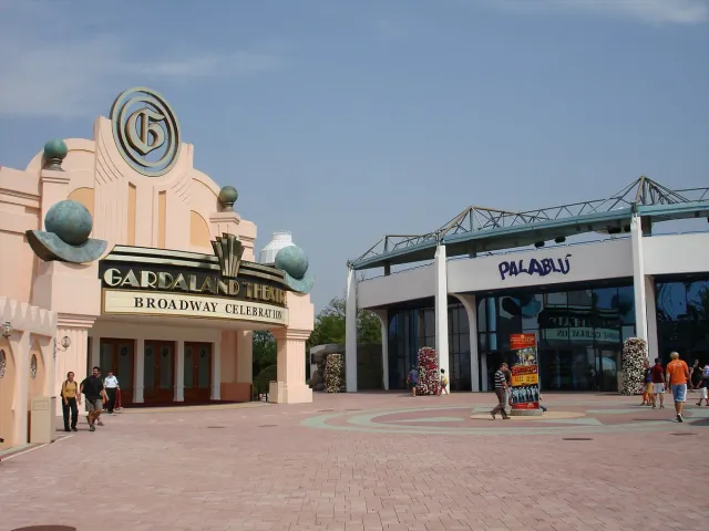 A paved entrance plaza with colourful buildings and visitors at a theme park