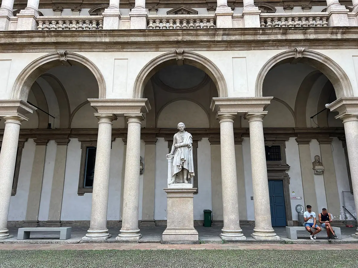 An inner courtyard with a row of arches and columns and a bronze statue on a plinth at its centre