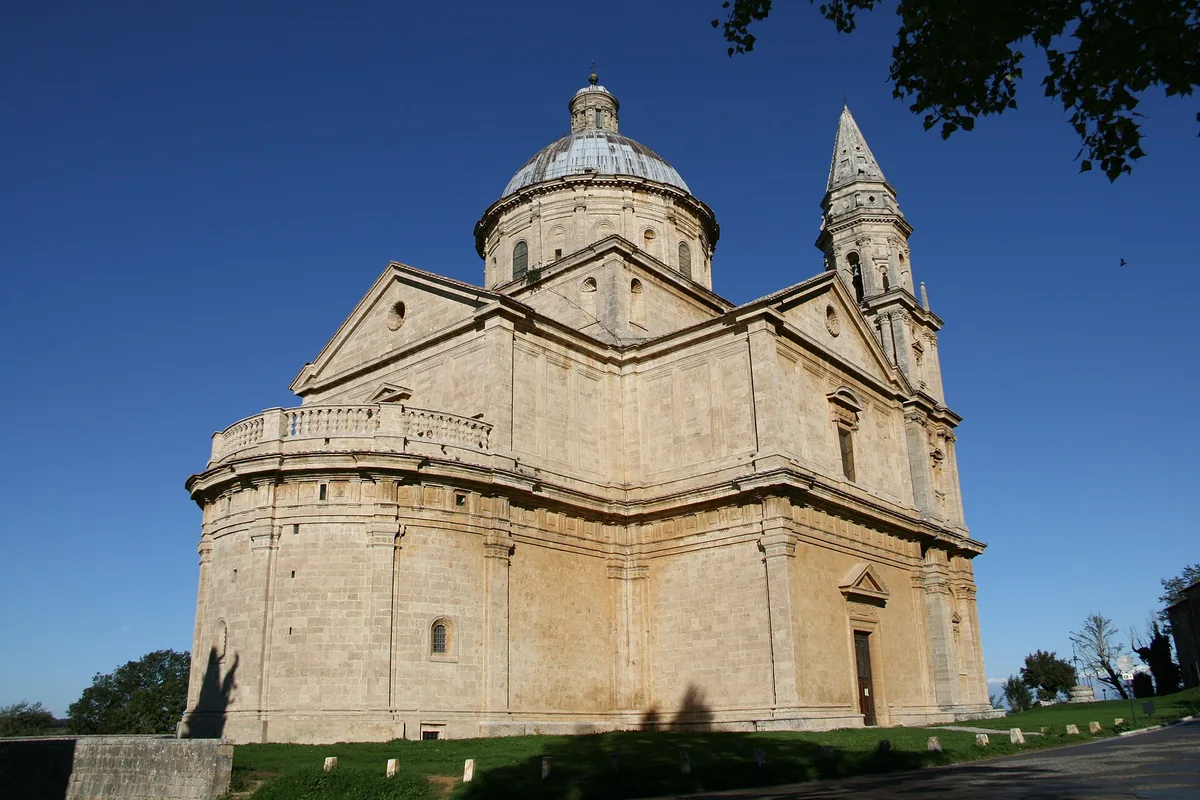 Pale stone church with a dome and a bell tower on a lawn under a blue sky