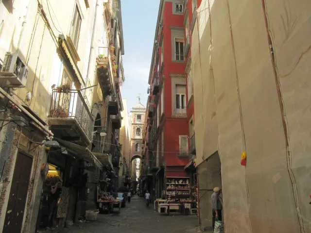 A narrow lane between tall houses lined with craft stalls and hanging wares