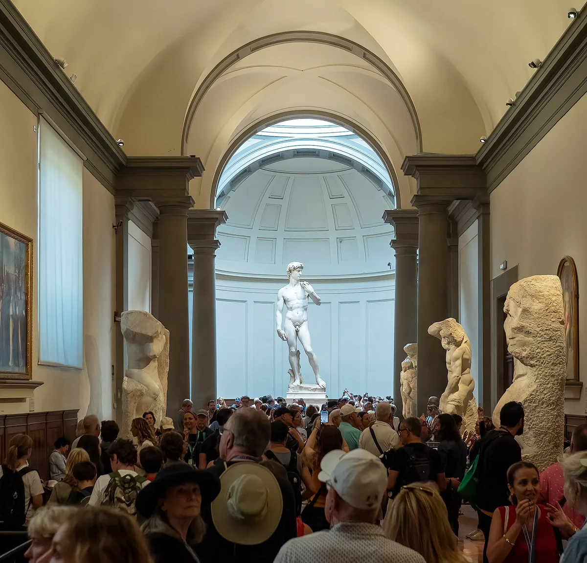 A marble standing figure beneath a lit dome at the end of a museum hall, with visitors in front