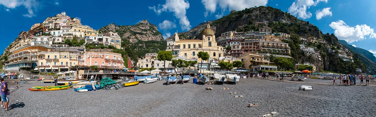 Pebble beach with colourful fishing boats and houses stacked up a steep hillside