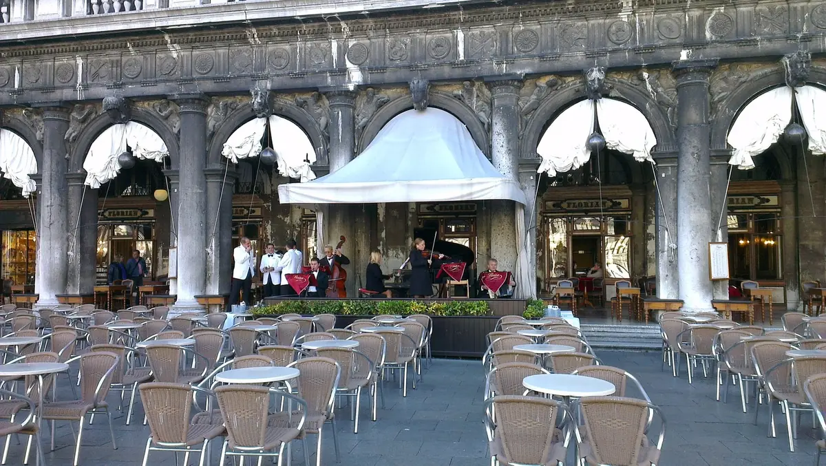 Round tables and cane chairs under a carved arcade with a small stage of musicians at the centre