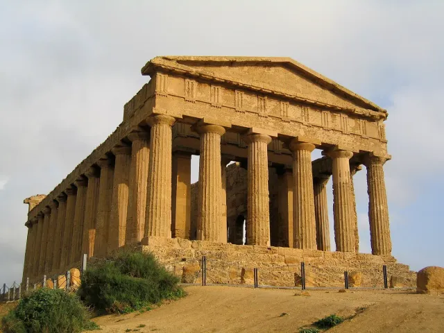 A golden stone Greek temple with rows of columns on an open ridge