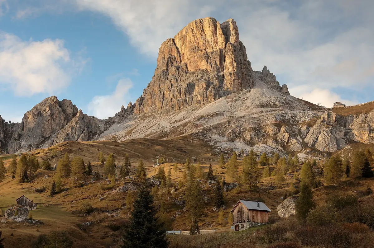 A wooden hut on an autumn grass slope beneath an isolated rock summit